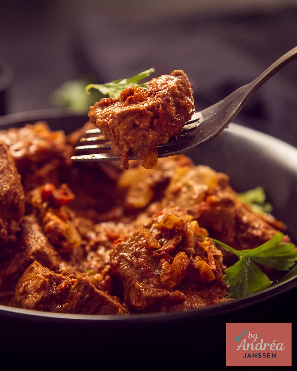 A black bowl with curry madras a fork taking out some meat.