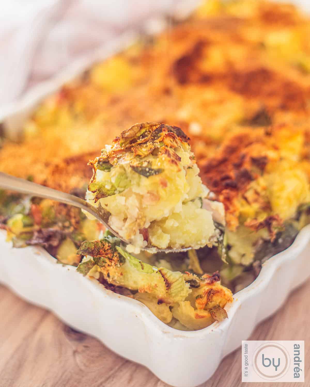 Een hoogtefoto met een deel van een witte ovenschaal met stamppot andijvie, met worst.