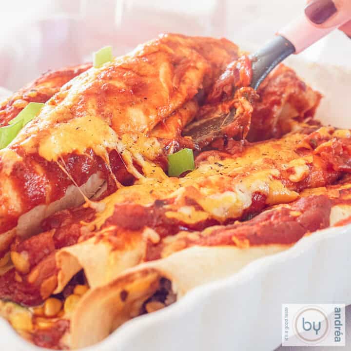 Een vierkante foto met een witte schaal met Mexicaanse enchilada's gevuld met gehakt, mais en tomatensaus en kaas.
