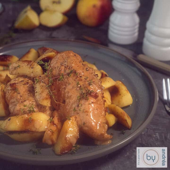 Een vierkante foto met een grijs bord met kipfilet met saus en appeltjes.