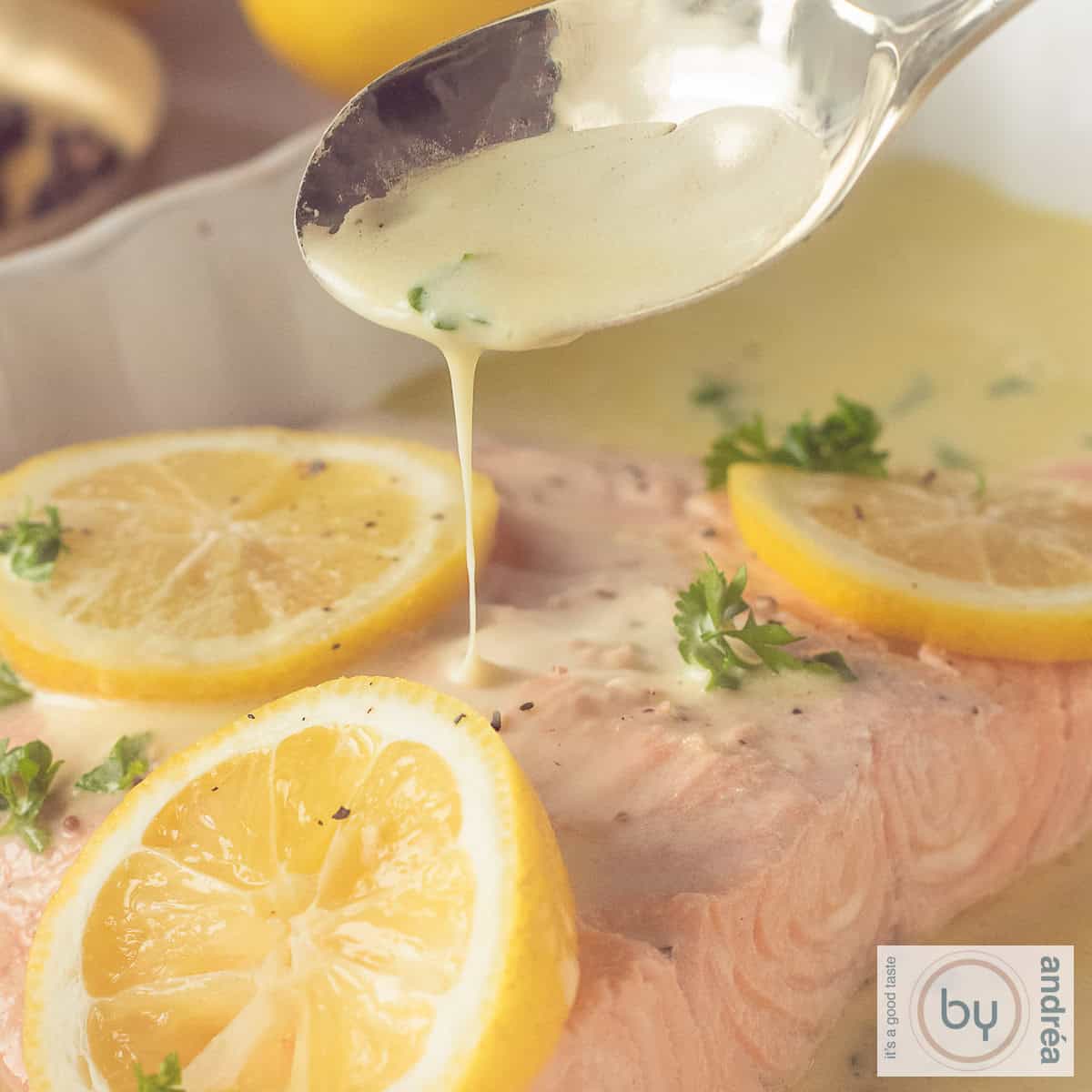Een vierkante foto met een moot zalm met schijfjes citroen, peterselie en witte wijn saus. Deze wordt met een lepel op de vis gegoten.