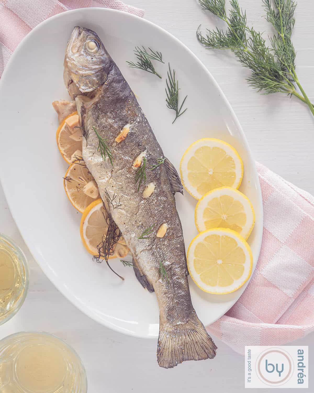Een foto van bovenaf van een wit bord met een zalmforel, gebakken in de oven, met citroen, dille en knoflook