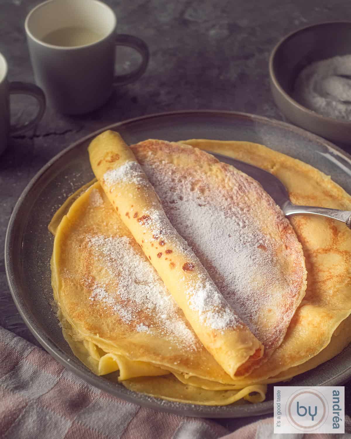 Een hoogtefoto van een stapel pannenkoeken met poedersuiker op een grijze ondergrond.