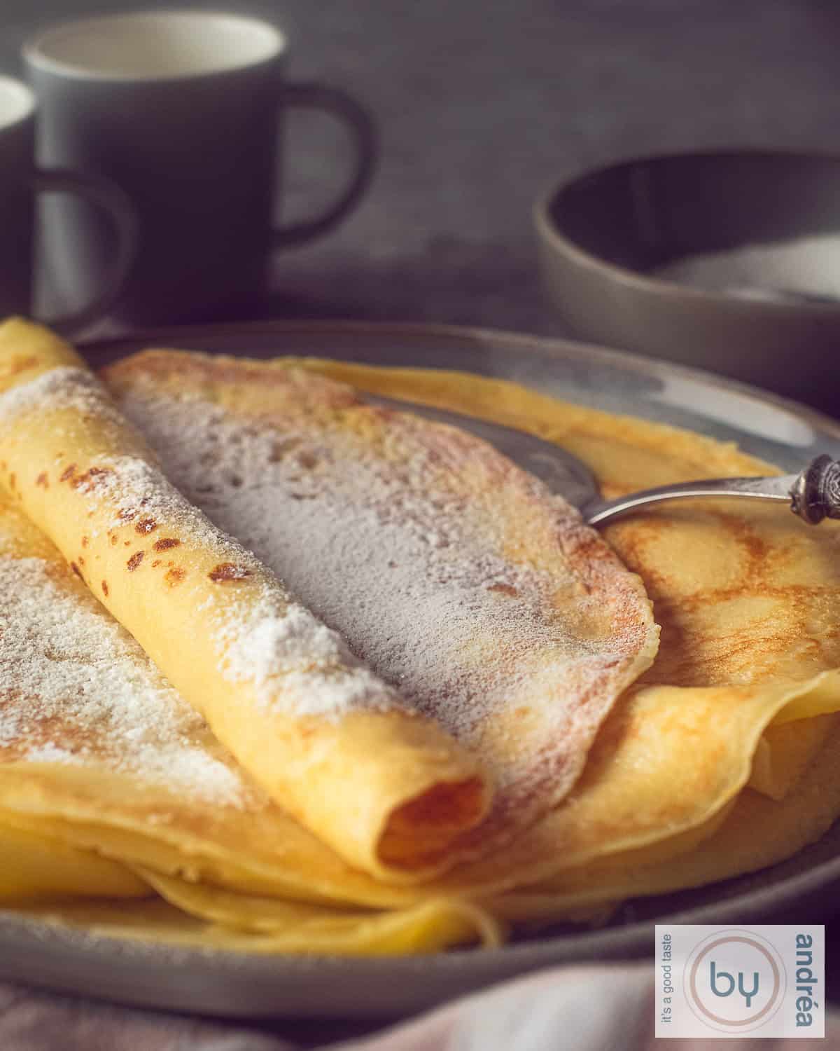 Een deel van een grijs bord met een stapel pannenkoeken, met poedersuiker. Een donkere achtergrond.