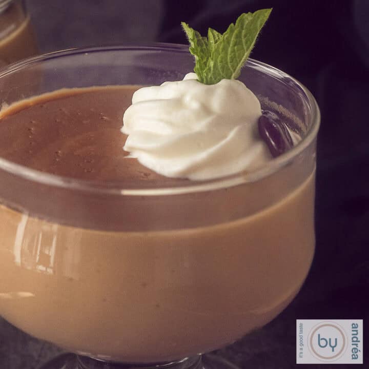 Een vierkante foto van een macro opname van hopjesvla met een toefjes slagroom, een chocolade koffieboon en munt.