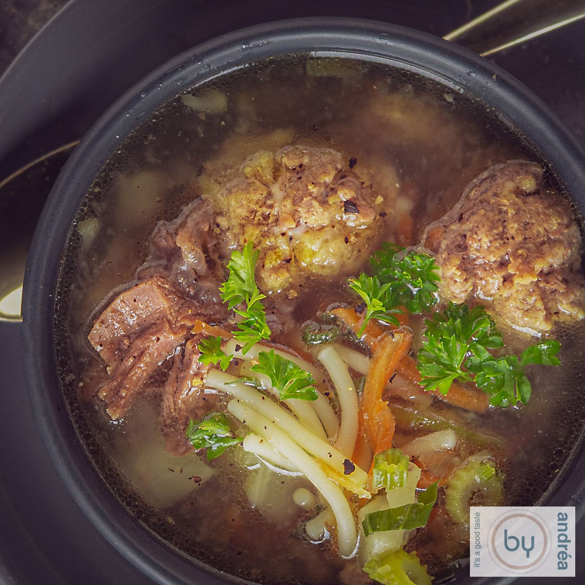 A square photo from above of vegetable soup with meatballs, vegetables, vermicelli and parsley.