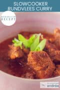 Een deel van een roze kom met rundvlees in een curry gemaakt in de slowcooker. Wat lente ui als garnering. Een tekst bovenin: makkelijk recept, slowcooker rundvlees curry