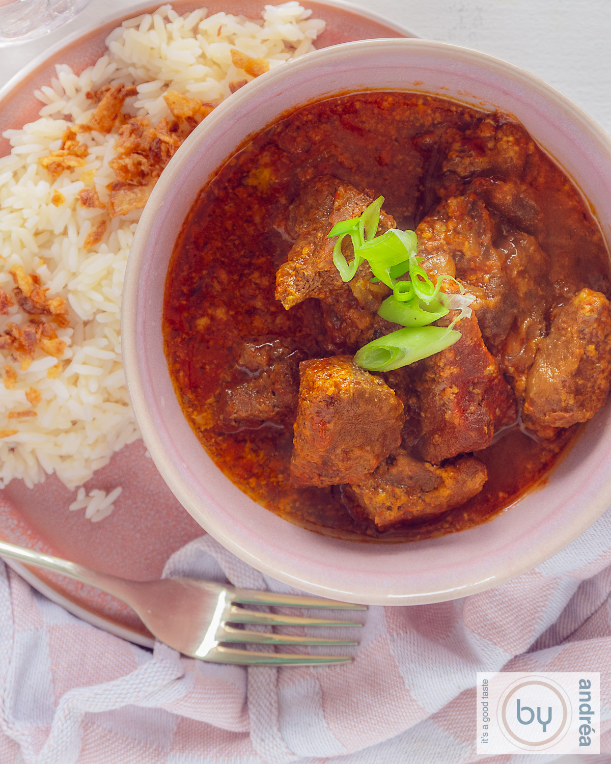 Een foto van bovenaf van een roze schaal met Slowcooker Rundvlees curry. Wat rijst ernaast.