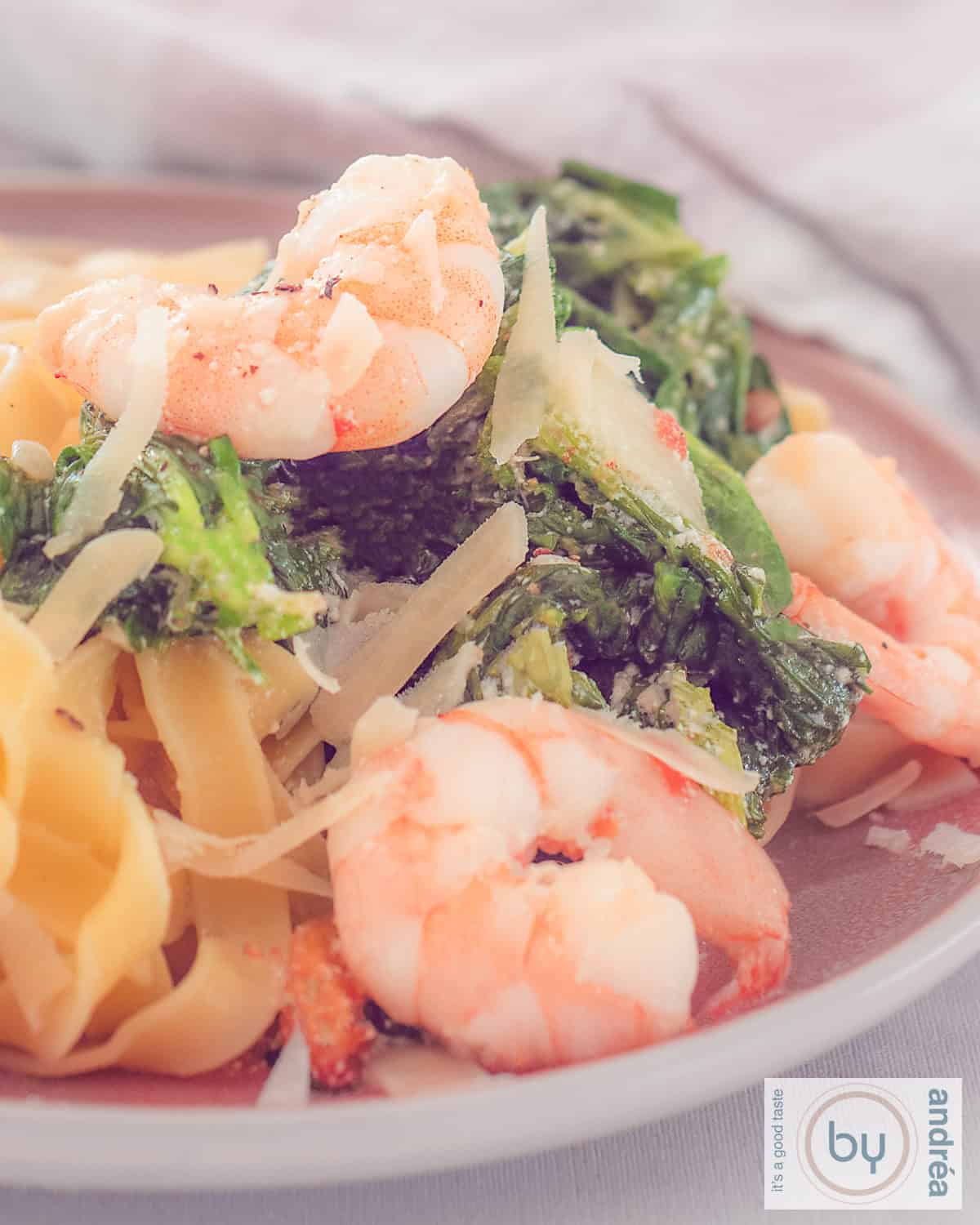 Een hoogtefoto met tagliatelle, garnalen en veldsla in een romige saus op een roze bord.