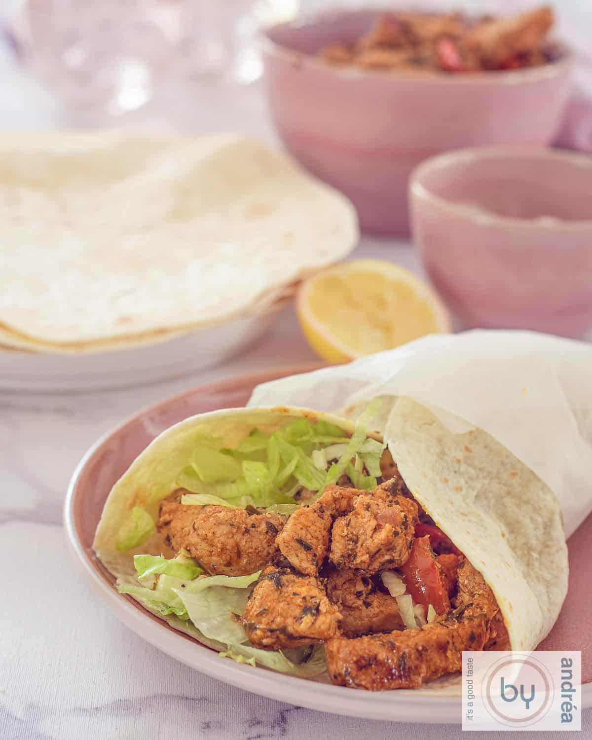 Een hoogtefoto: een wrap gevuld met gyros vlees en sla. In de achtergrond, wraps en schaaltjes met bijgerechten.