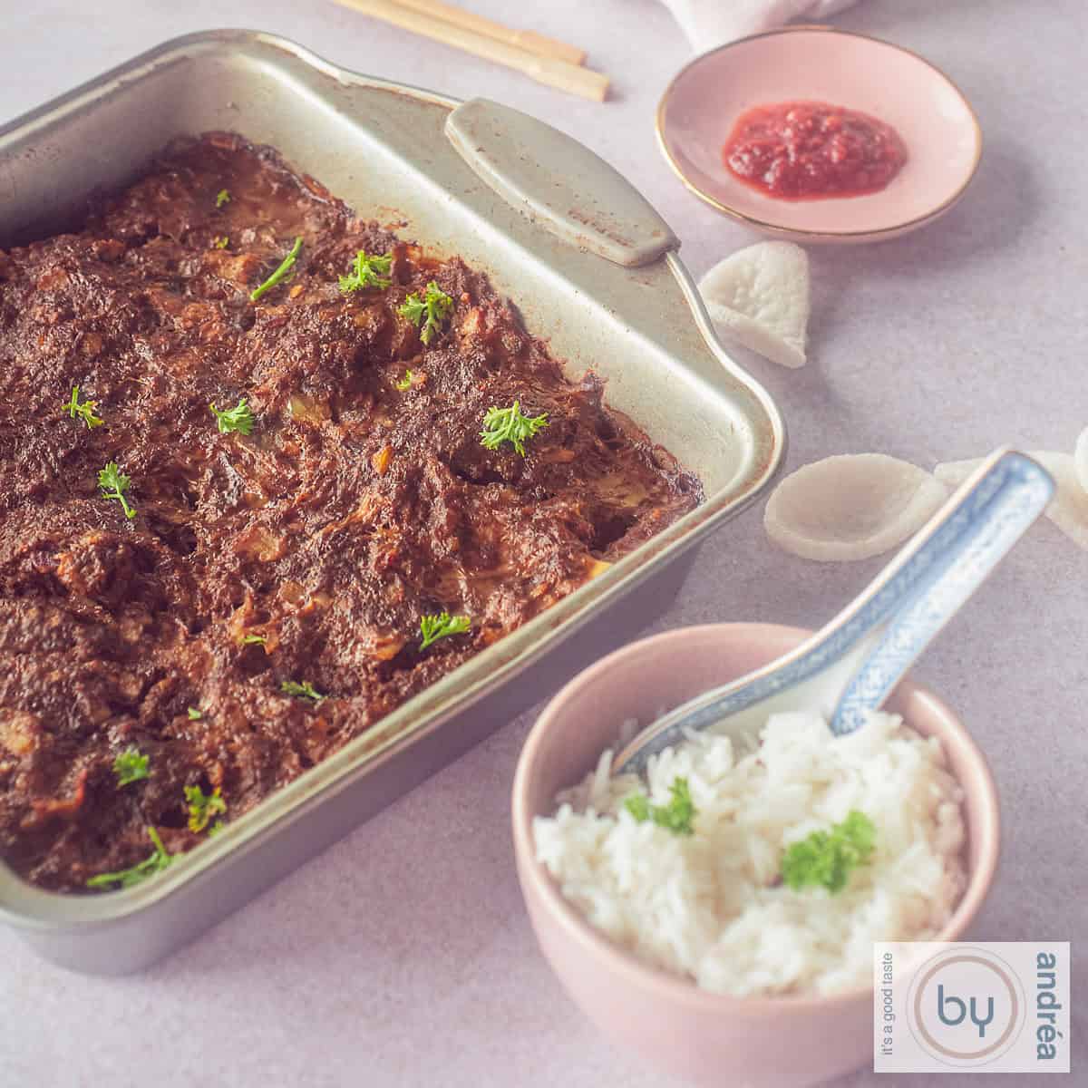Een vierkante foto met een bakblik gevuld met frikadel pan, een roze kom met witte rijst en een schaaltje met sambal.