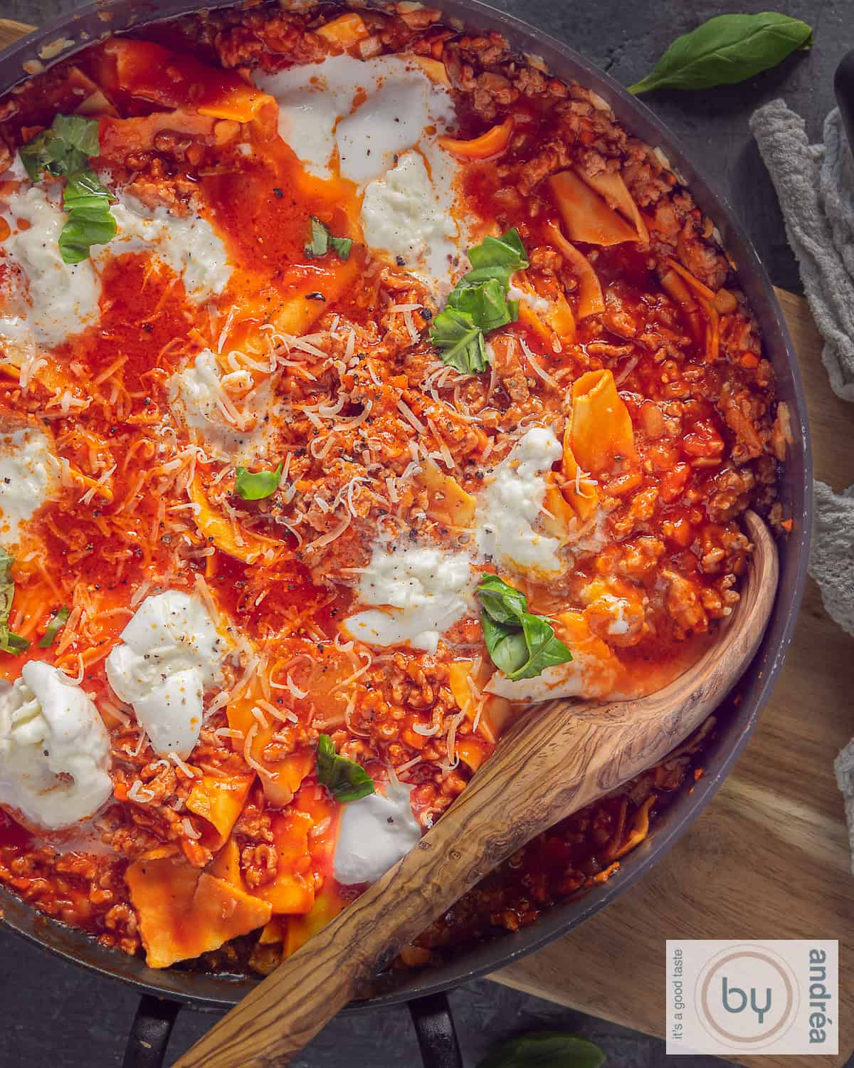 Een foto van bovenaf van een pan gevuld met lasagnette. Een houten lepel ligt in de pan.