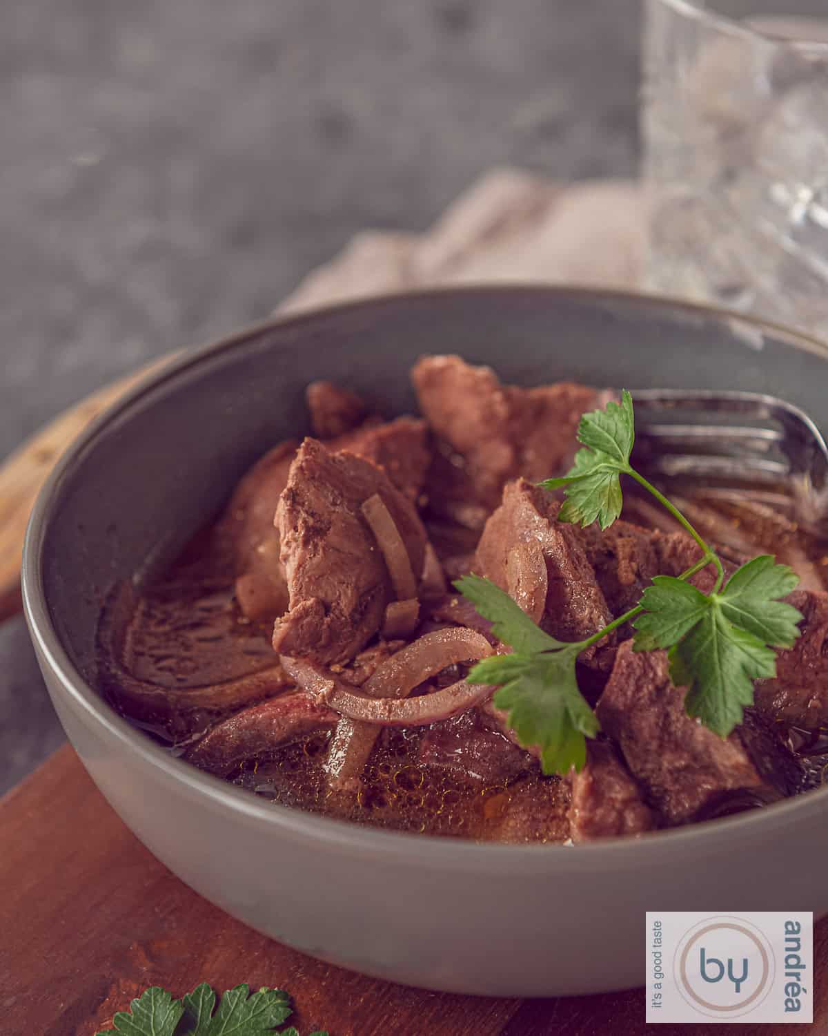 Een grijze kom met blokjes entrecote, ui en een heerlijke saus. Gegarneerd met peterselie.