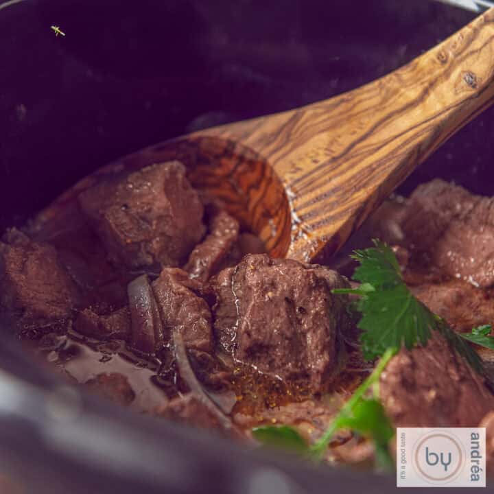 Een vierkante foto met een deel van een slowcooker waarin entrecote met botersaus zit.