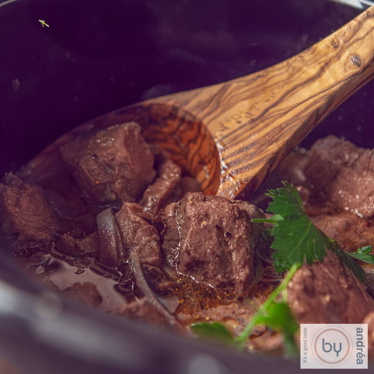 Een vierkante foto met een deel van een slowcooker waarin entrecote met botersaus zit.