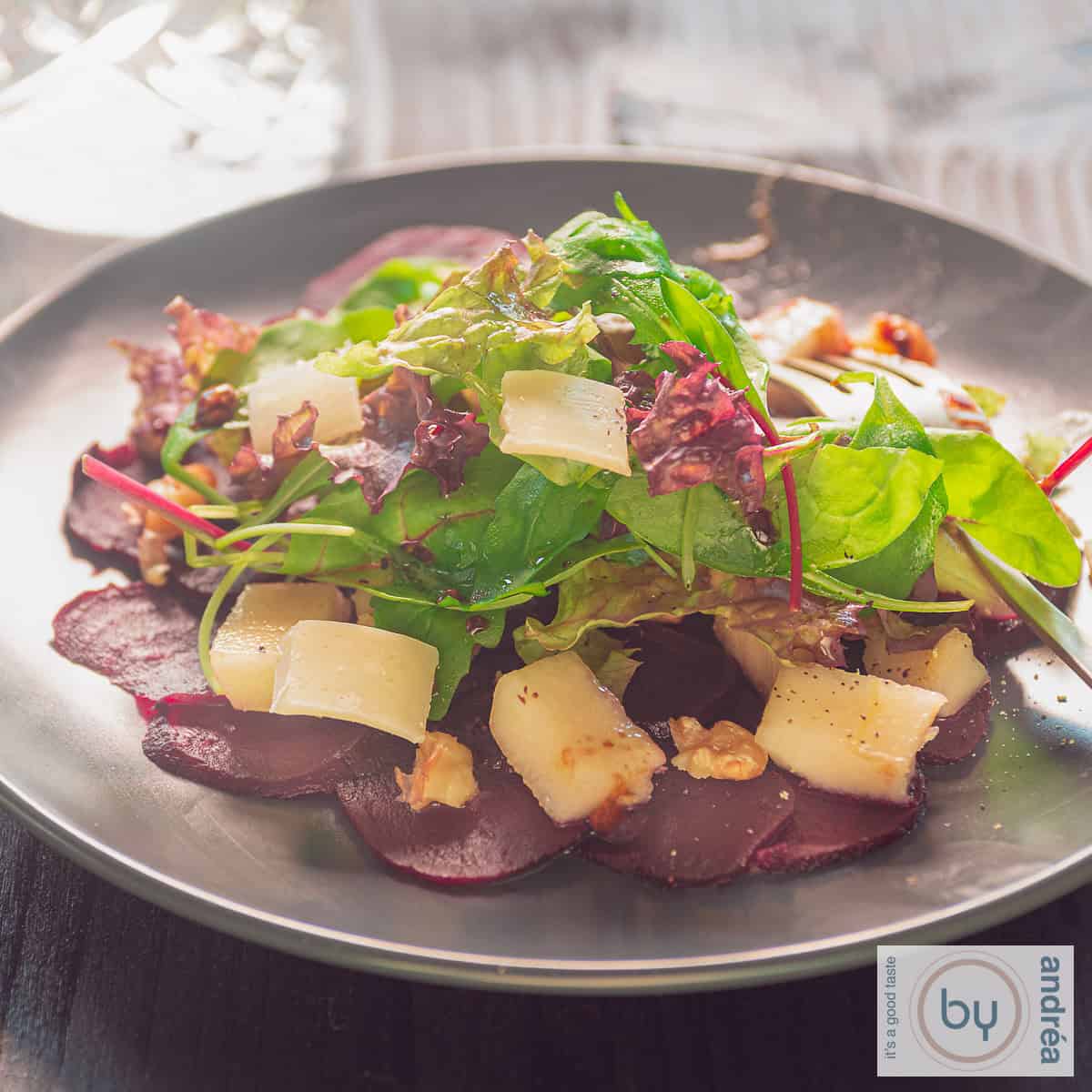 Carpaccio van bieten met peer, sla, nootjes en dressing op een grijs bord