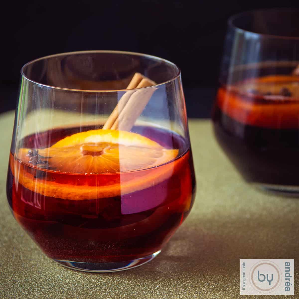 Een vierkante foto met twee glazen met bisschopswijn op een gouden ondergrond