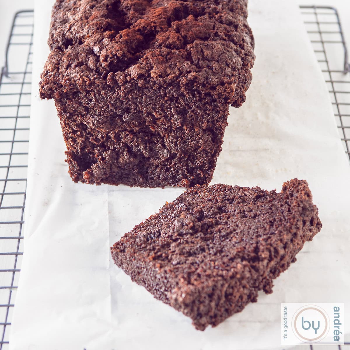 Een vierkante foto met een deel van een chocolade courgette cake waar een plakje vanaf is gesneden