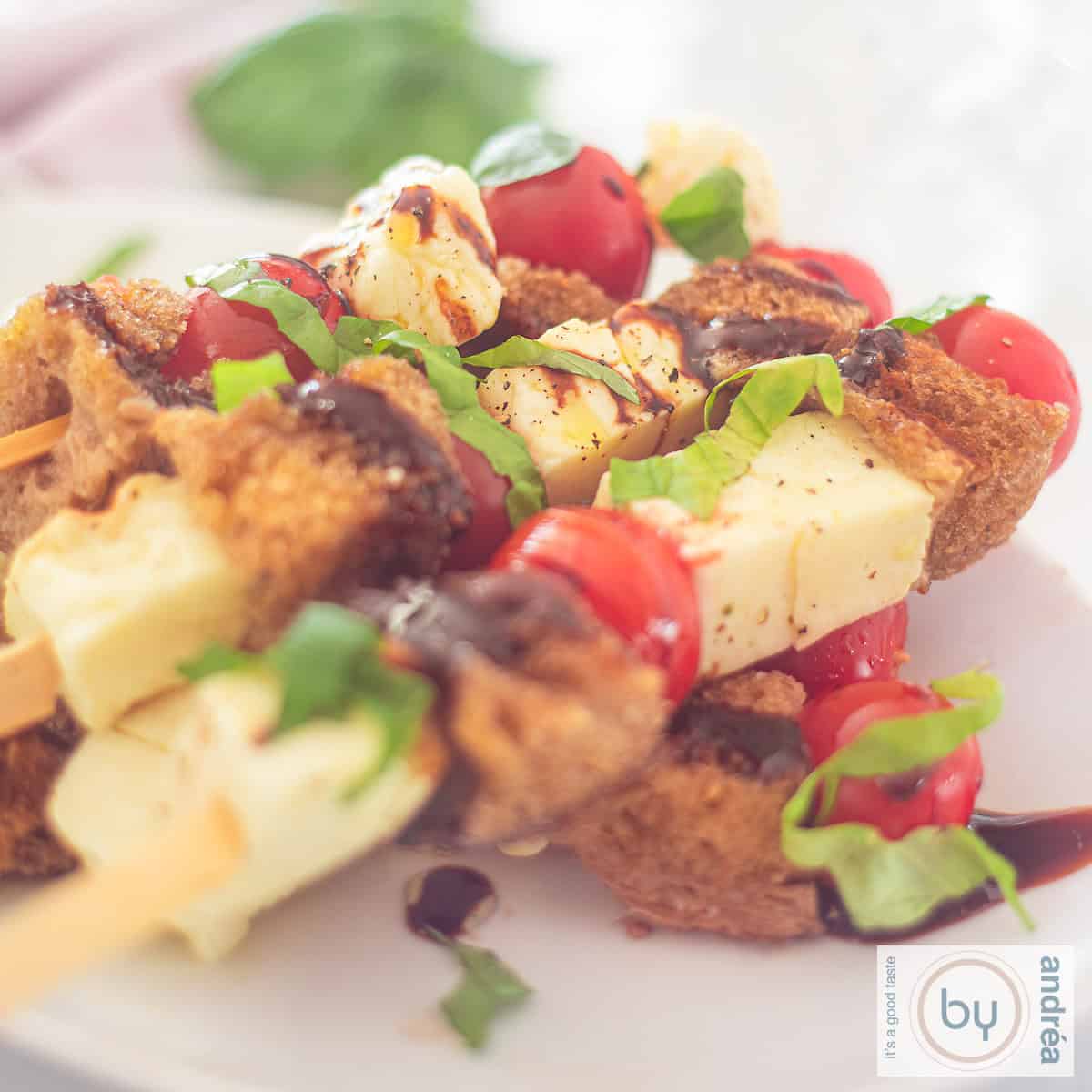 Een bord met spiesen met halloumi, cherrytomaten en brood met balsamicoazijn
