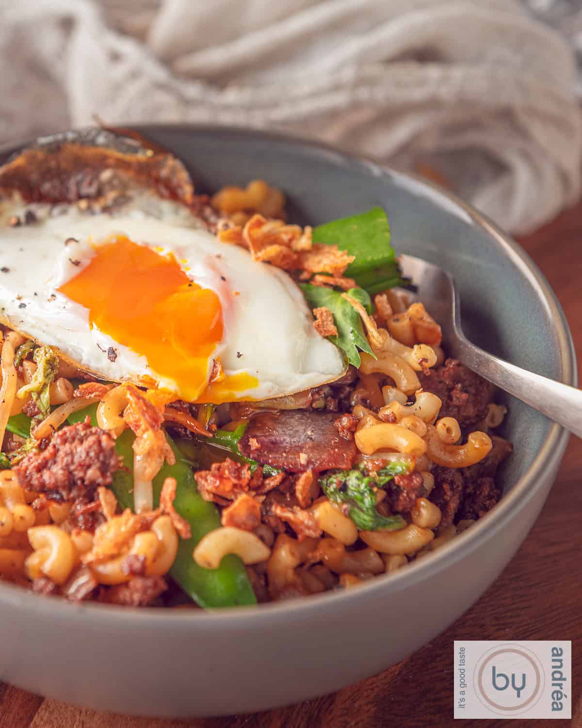 Een grijze schaal gevuld met Indonesische stijl macaroni met gehakt, groente en een spiegelei