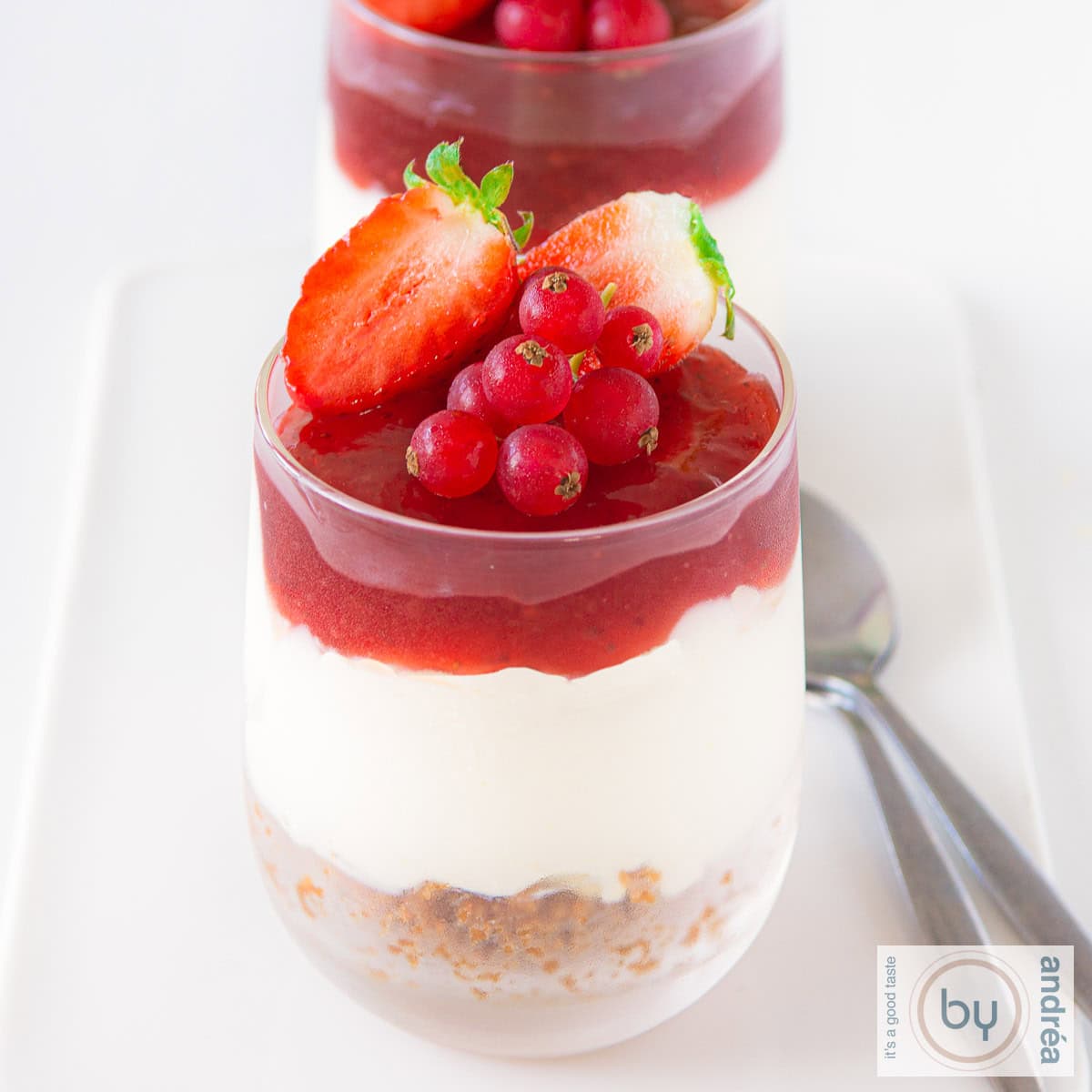 Een glas gevuld met no bake cheesecake met rode vruchten op een wit schaaltje