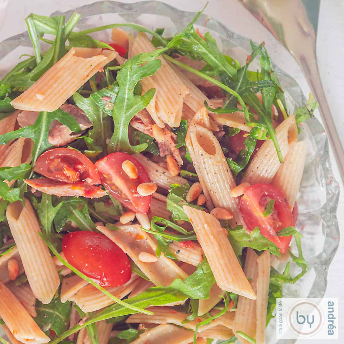 Een vierkante foto met een penne pastasalade met gerookte makreel en cherry tomaatjes