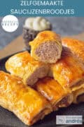 Een grijze schaal vol met saucijzenbroodjes waarvan er een is dorogesneden. Een tekst bovenin: makkelijk recept, zelfgemaakte saucijzenbroodjes