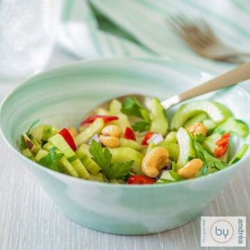 Een vierkante foto van een bakje met pittige komkommer salade met peper en cashewnoten