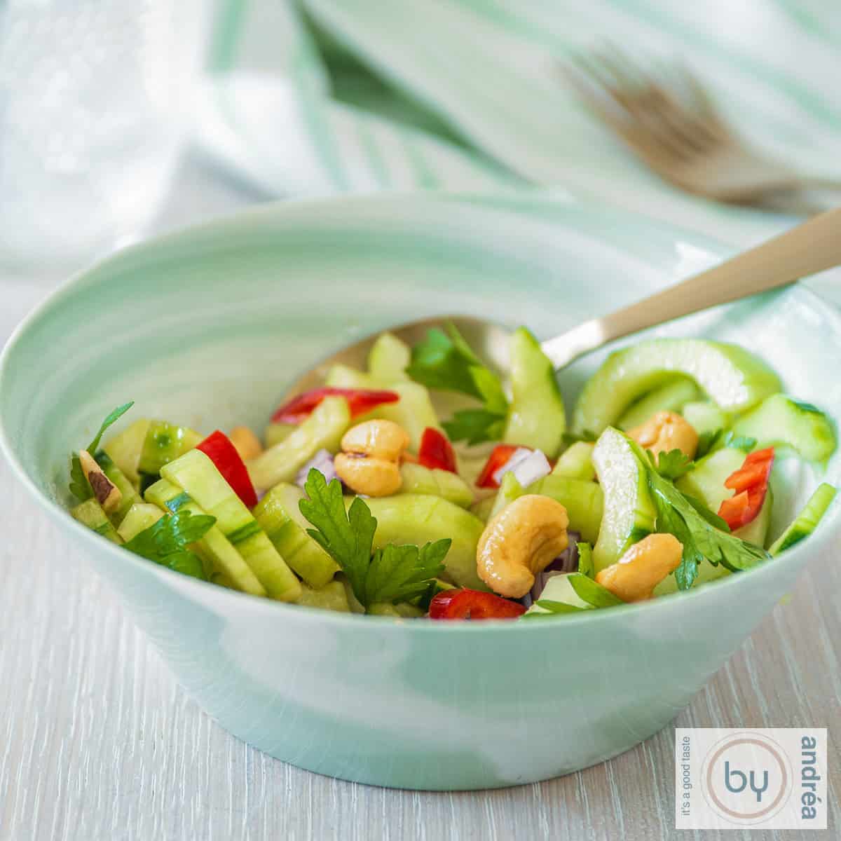 Een vierkante foto van een bakje met pittige komkommer salade met peper en cashewnoten