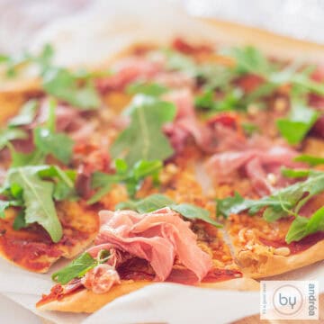 Een vierkante foto met een pizza met Parmaham en rucola