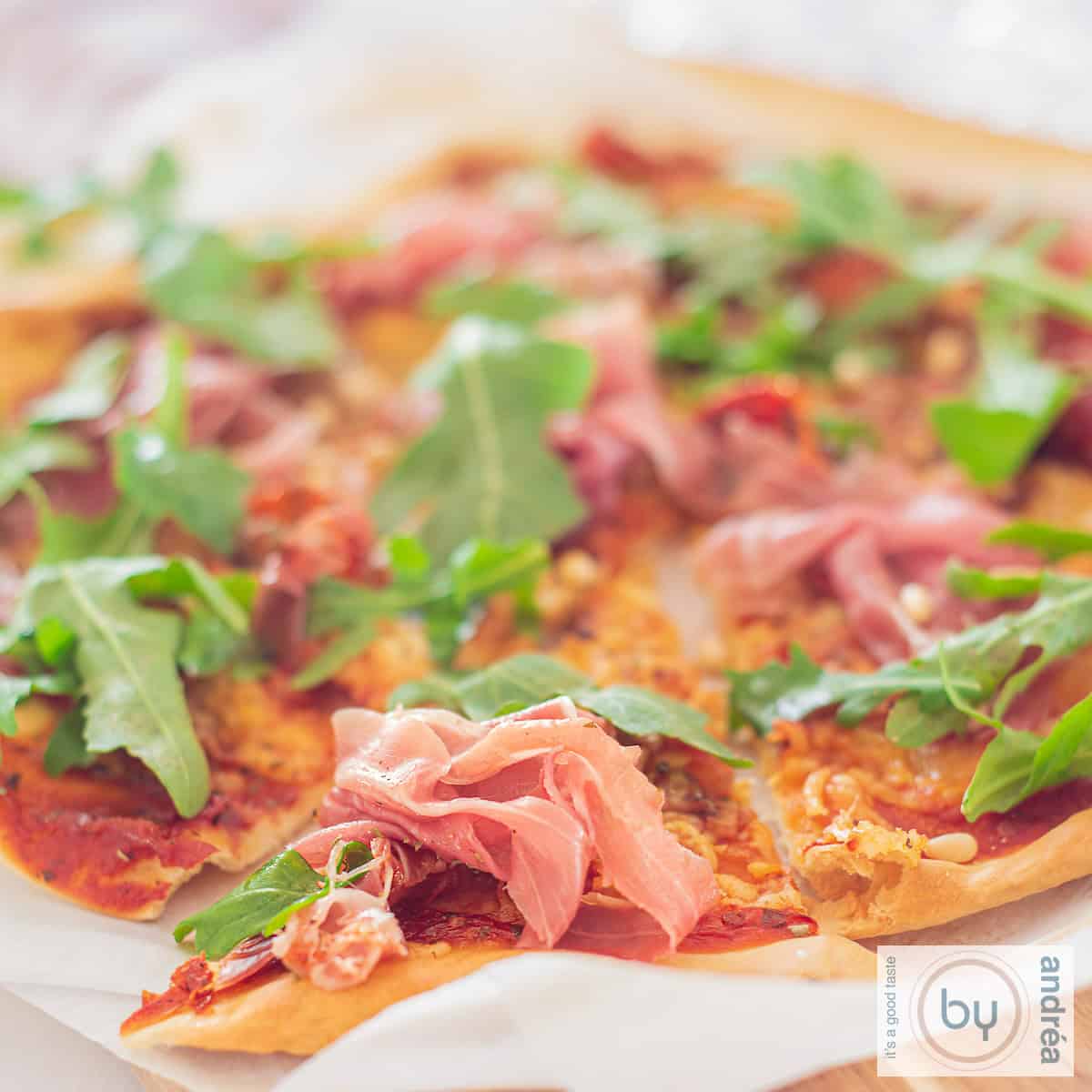 Een vierkante foto met een pizza met Parmaham en rucola