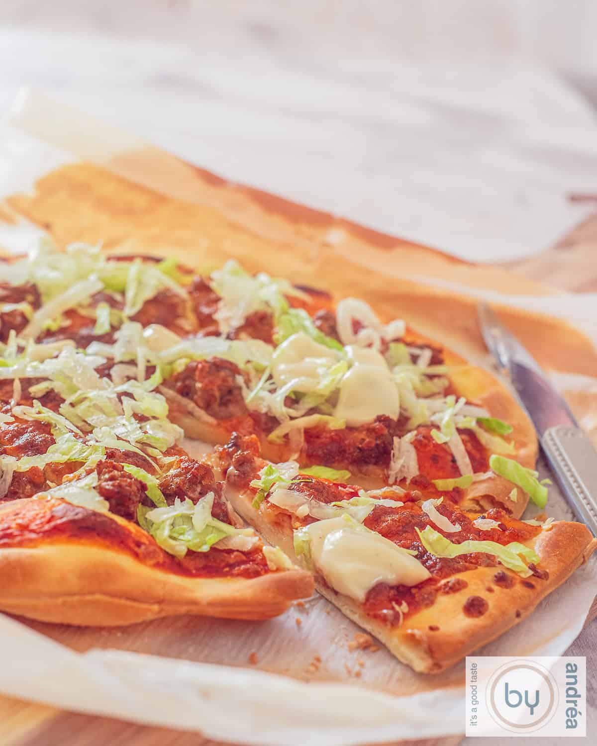 Een pizza met een punt uitgesneden met taco gehakt, ijsbergsla en knoflooksaus op een houten plank.