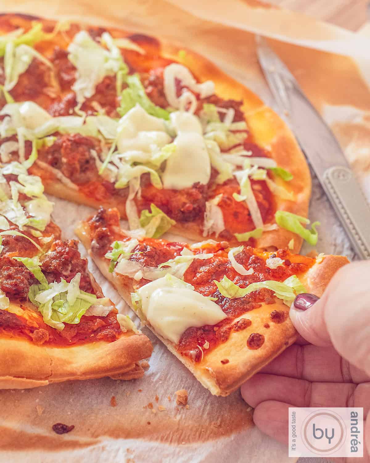 Een pizza taco met ijsbergsla en knoflooksaus. Een hand pakt een punt.