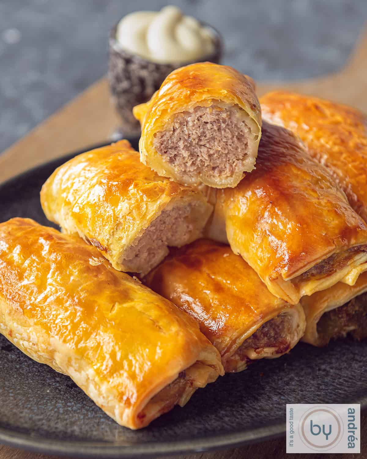 Een schaal met saucijzenbroodjes, de bovenste gehalveerd, gehakvulling zichtbaar