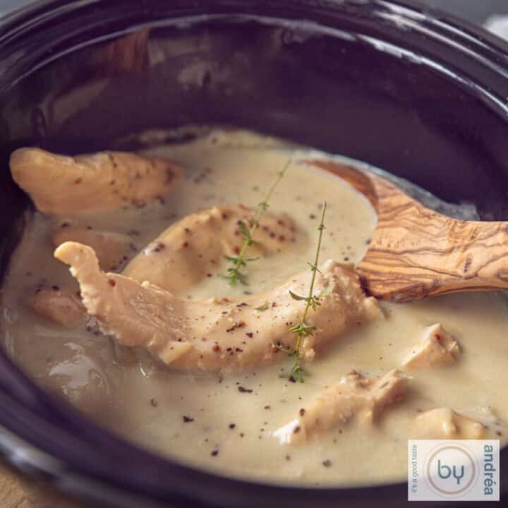 Een vierkante foto met een slowcooker gevuld met kip en mosterdsaus