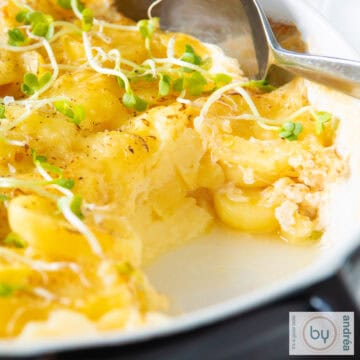 Een vierkante foto met een zwarte schaal gevuld met aardappelgratin met Emmentaler