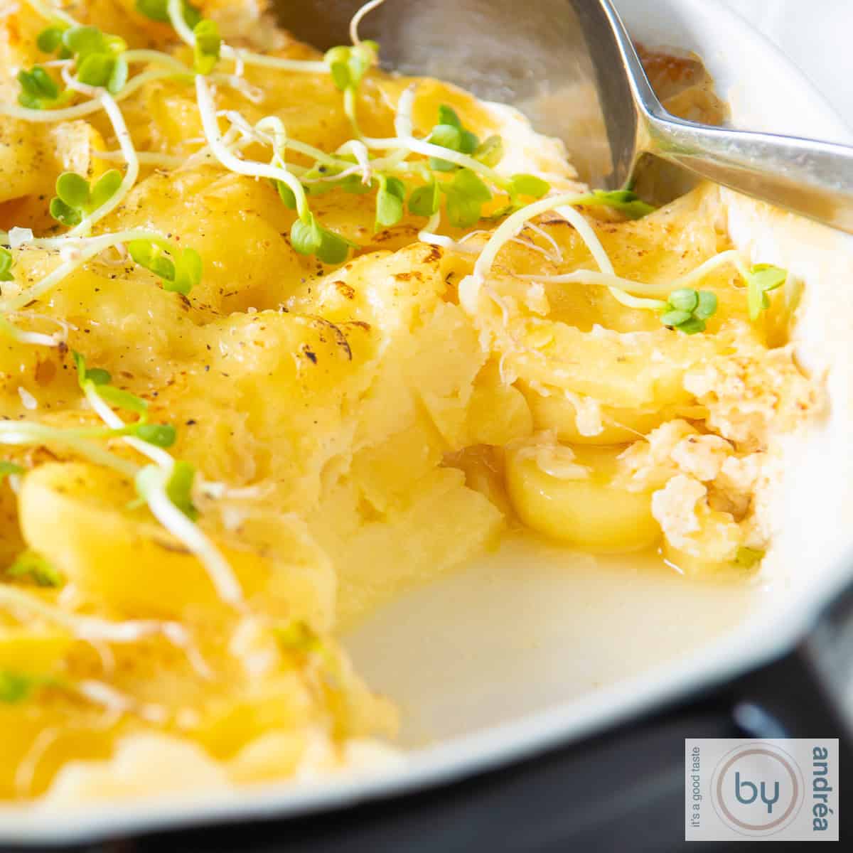 Een vierkante foto met een zwarte schaal gevuld met aardappelgratin met Emmentaler