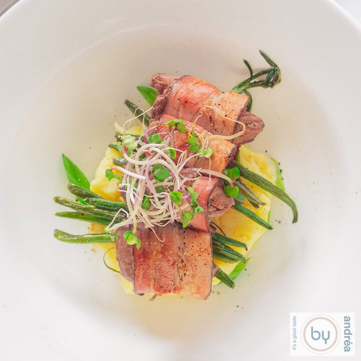 Een diep brod met aardappelpuree, haricot verts gerold in spek en hertenbiefstuk