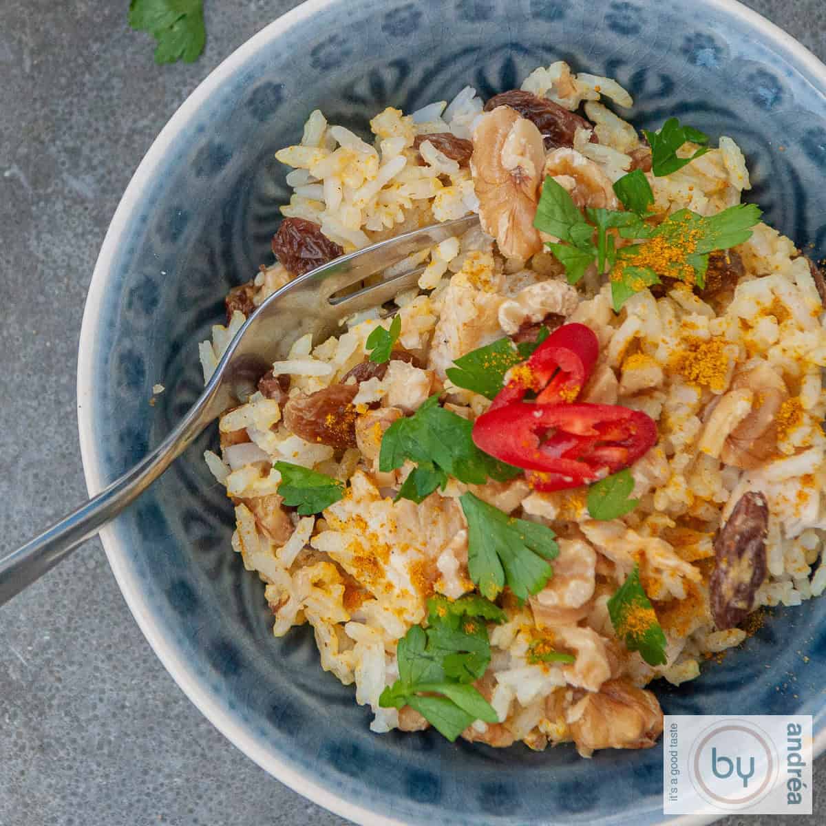 Een vierkante foto met een rijstsalade met blokjes kip, kerrie en walnoten