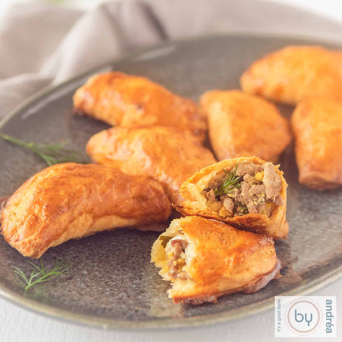 Een vierkante foto met een schaal met pirozhki gevuld met gekruid gehakt