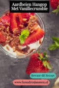 Een foto van bovenaf van een glazen schaal met hangop, aardbeien, gemarineerd en vanille crumble. Tekst: Aardbeien hangop met vanillecrumble