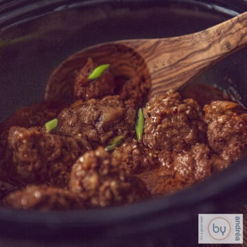 Een vierkante foto van een slowcooker gevuld met Indonesische gehaktballetjes in ketjapsaus