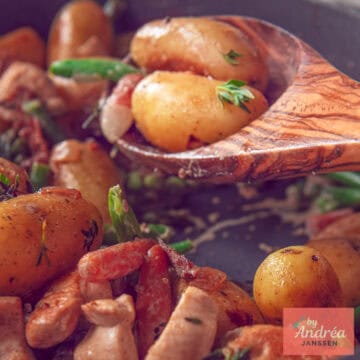 Een vierkante foto met een houten lepel met aardappels, groenten en kip