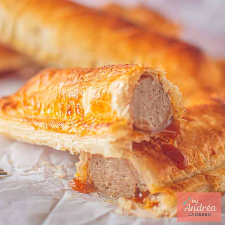 Een vierkant met frikandelbroodjes waar er een van is doorgesneden waar je frikandel bladerdeeg en curry lagen zieet.