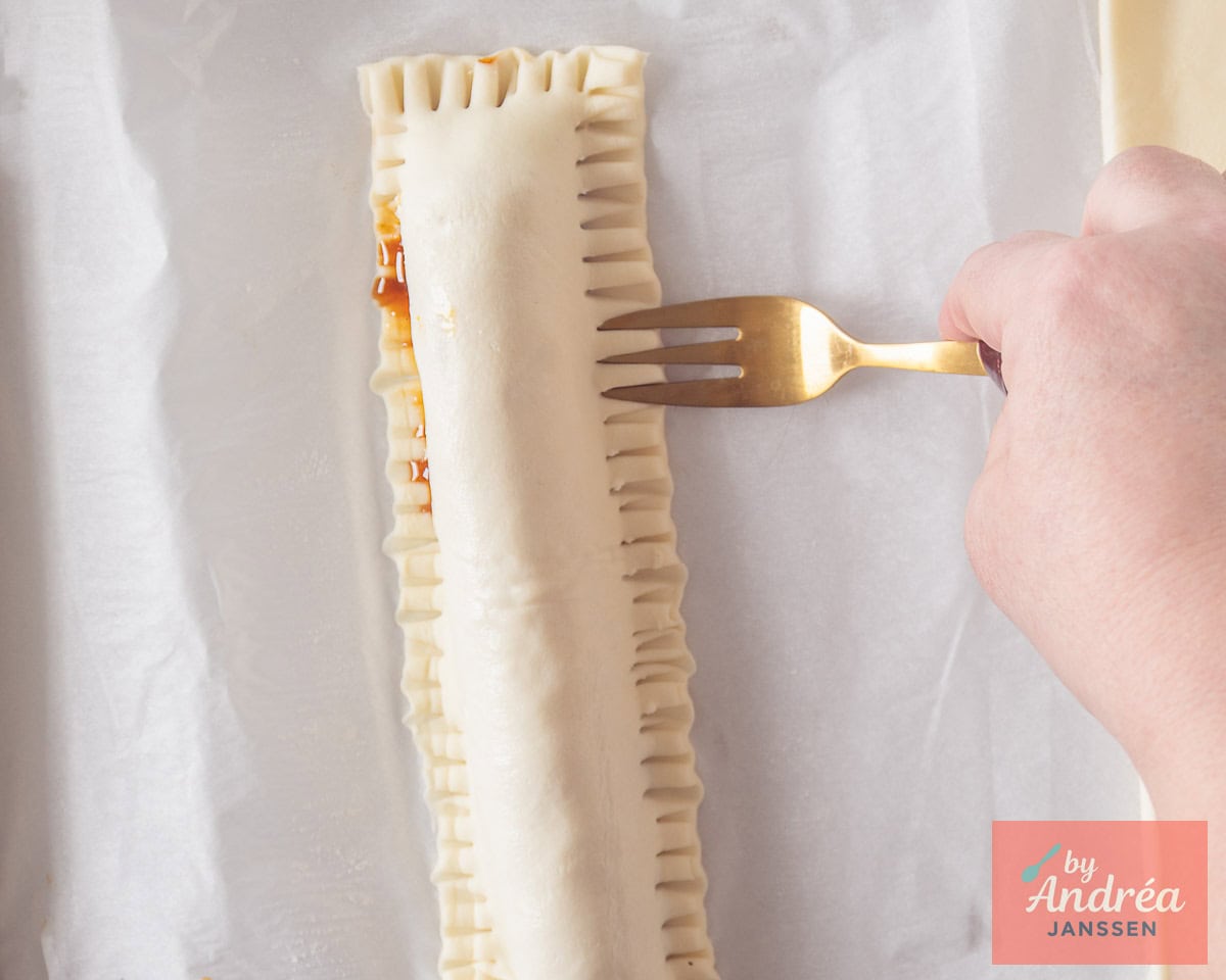 Een frikandelbroodje waar de randen worden dichtgedrukt met een vork