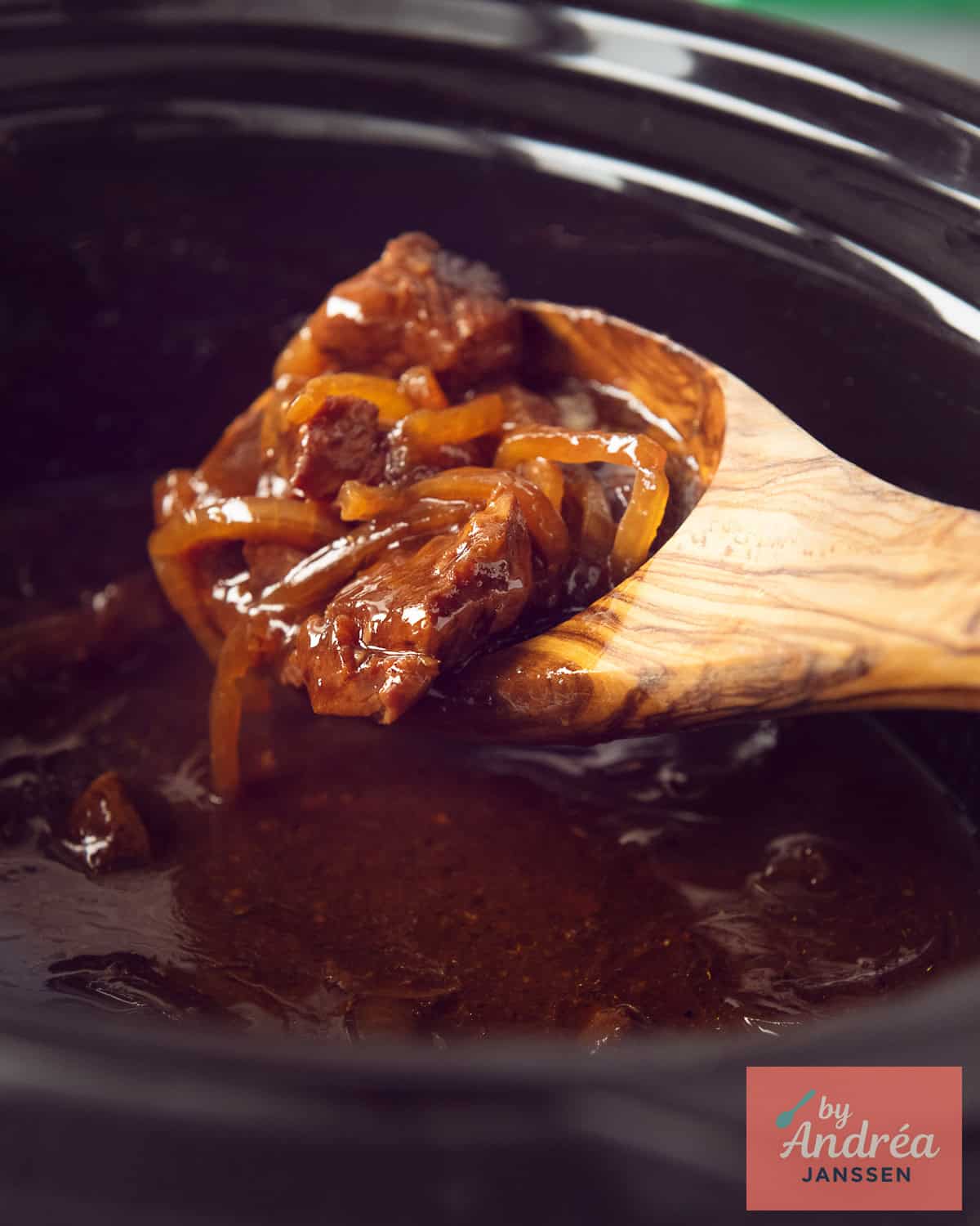 Een slowcooker waar een houten lepel stoofvlees schept