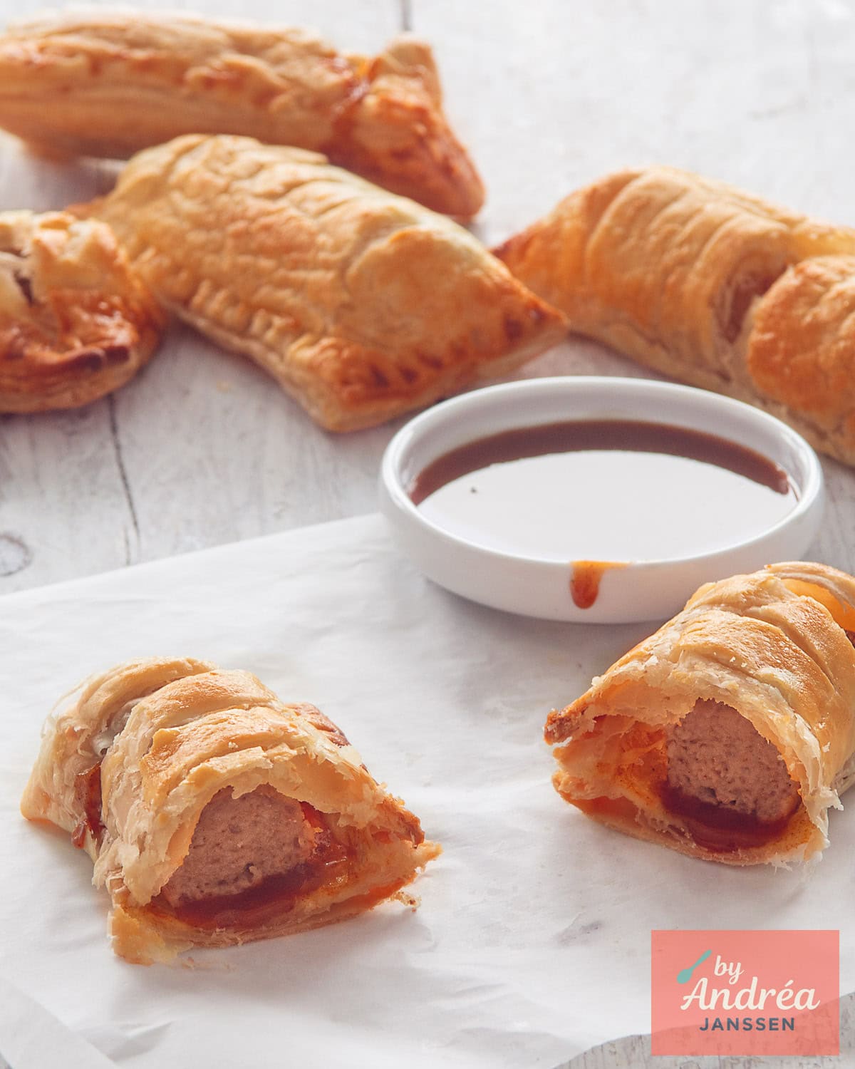 Een witte ondergrond met frikandelbroodjes. Voorin een frikandelbroodje met frikandel zichtbaar.