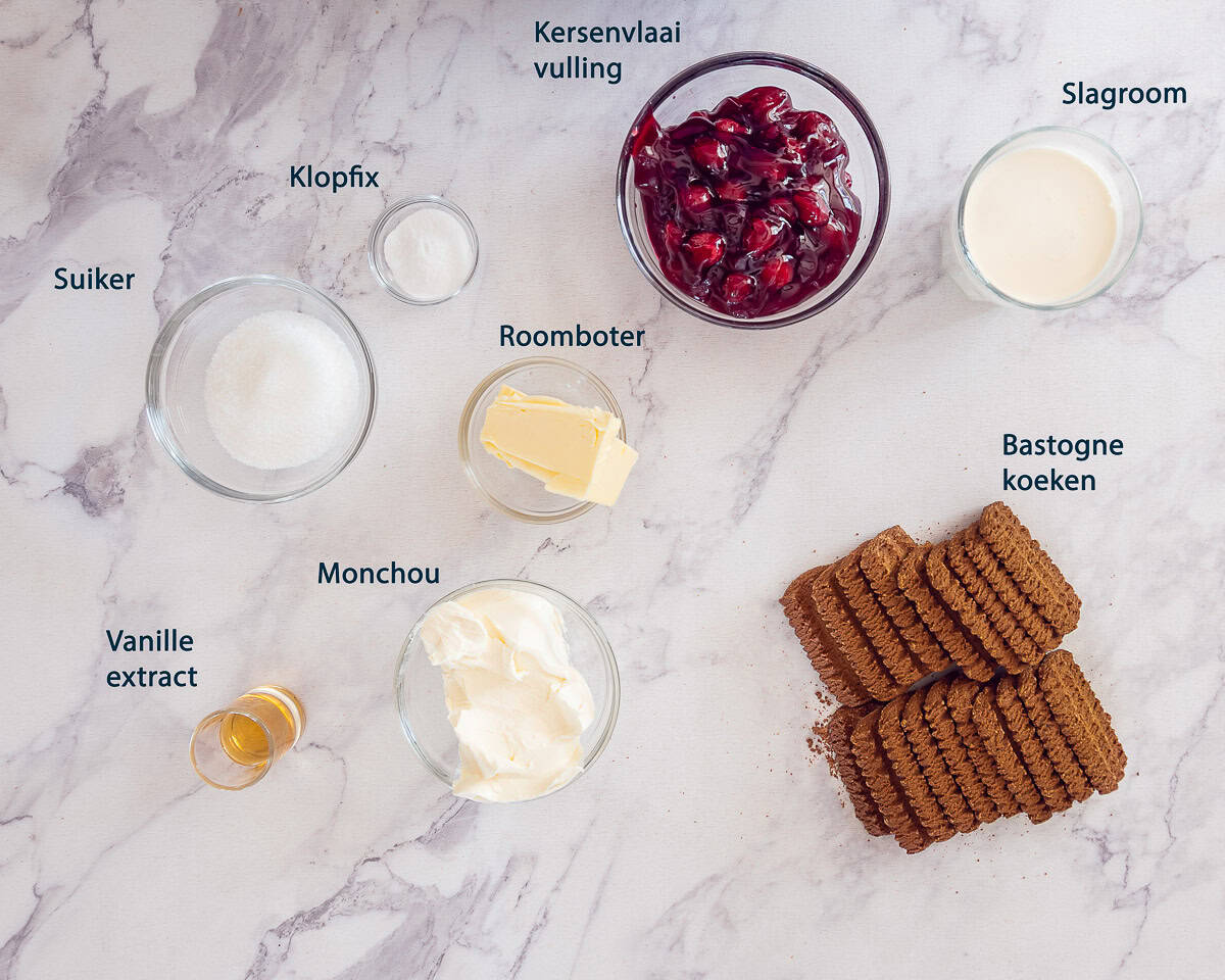 Ingredienten Monchoutaart met Bastogne en Kersentopping op een wit marmeren ondergrond met tekstbeschrijving