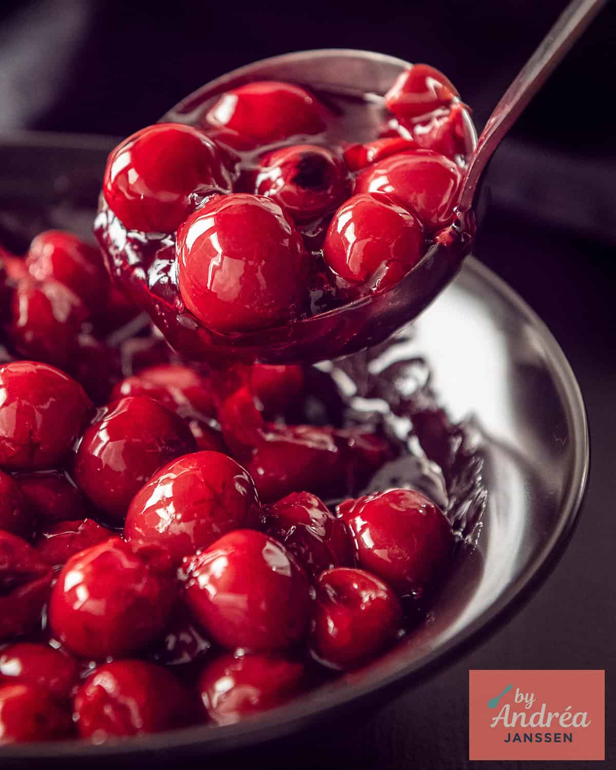 Een zwarte schaal met een vulling van kersen voor vlaai, monchou taart en dessert. Een lepel pakt een schep eruit.