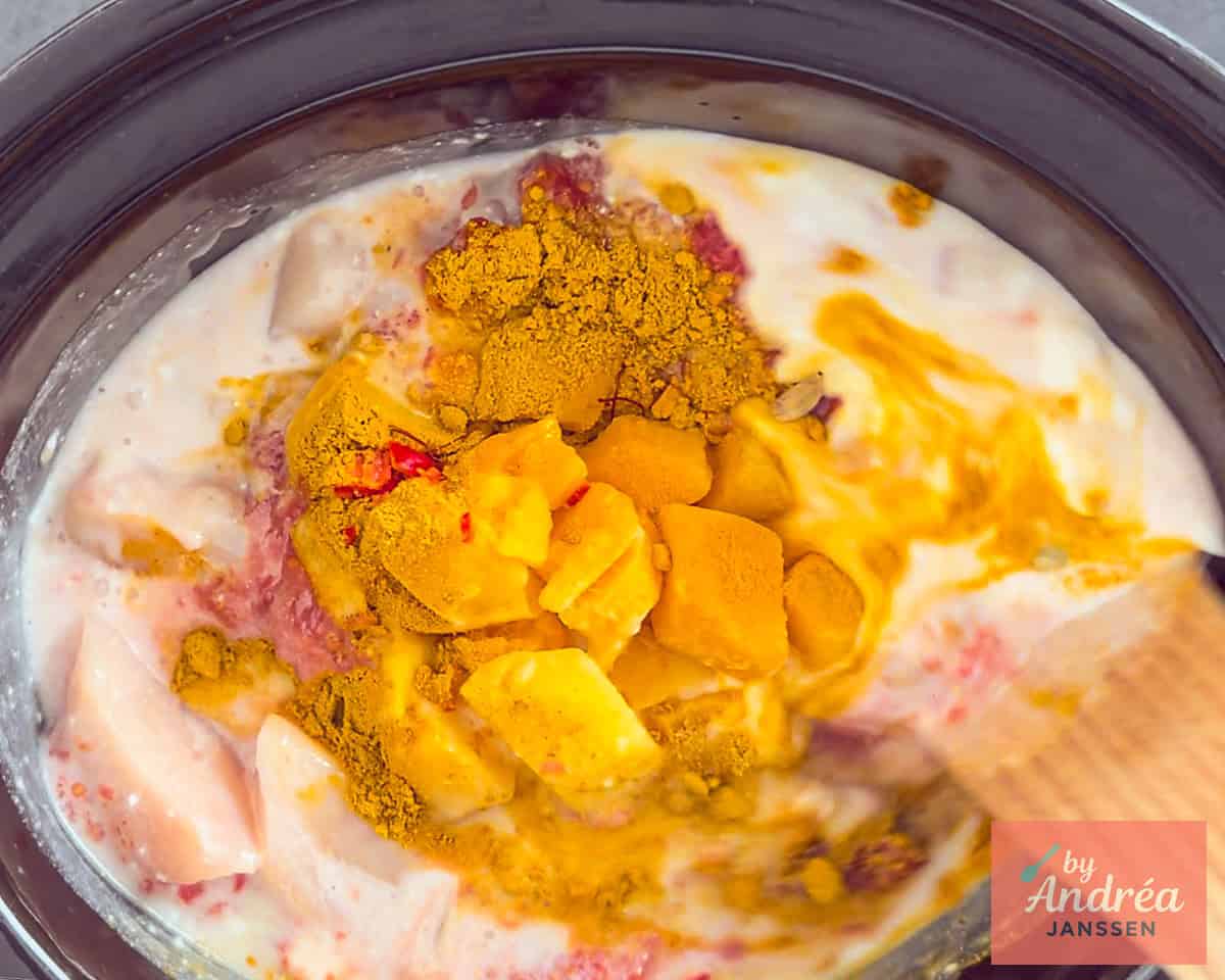 Een slowcooker met kip, kruiden, tomaten en kokosmelk en mango